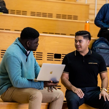 two students talk while sitting on bench at Bloch School