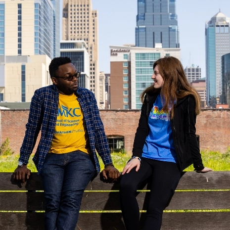 three students lean on a fence with the Kauffman Center in the skyline behind them