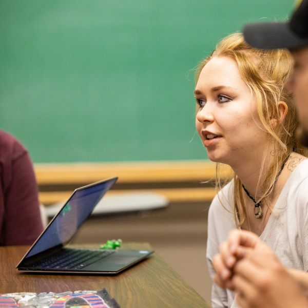 student listens attentively in classroom. A laptop is on the table.