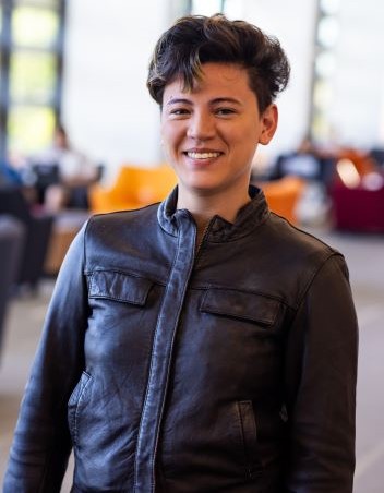 A PhD student wears a leather coat and stands with a smile on her face at the 威尼斯人娱乐城 Student Union