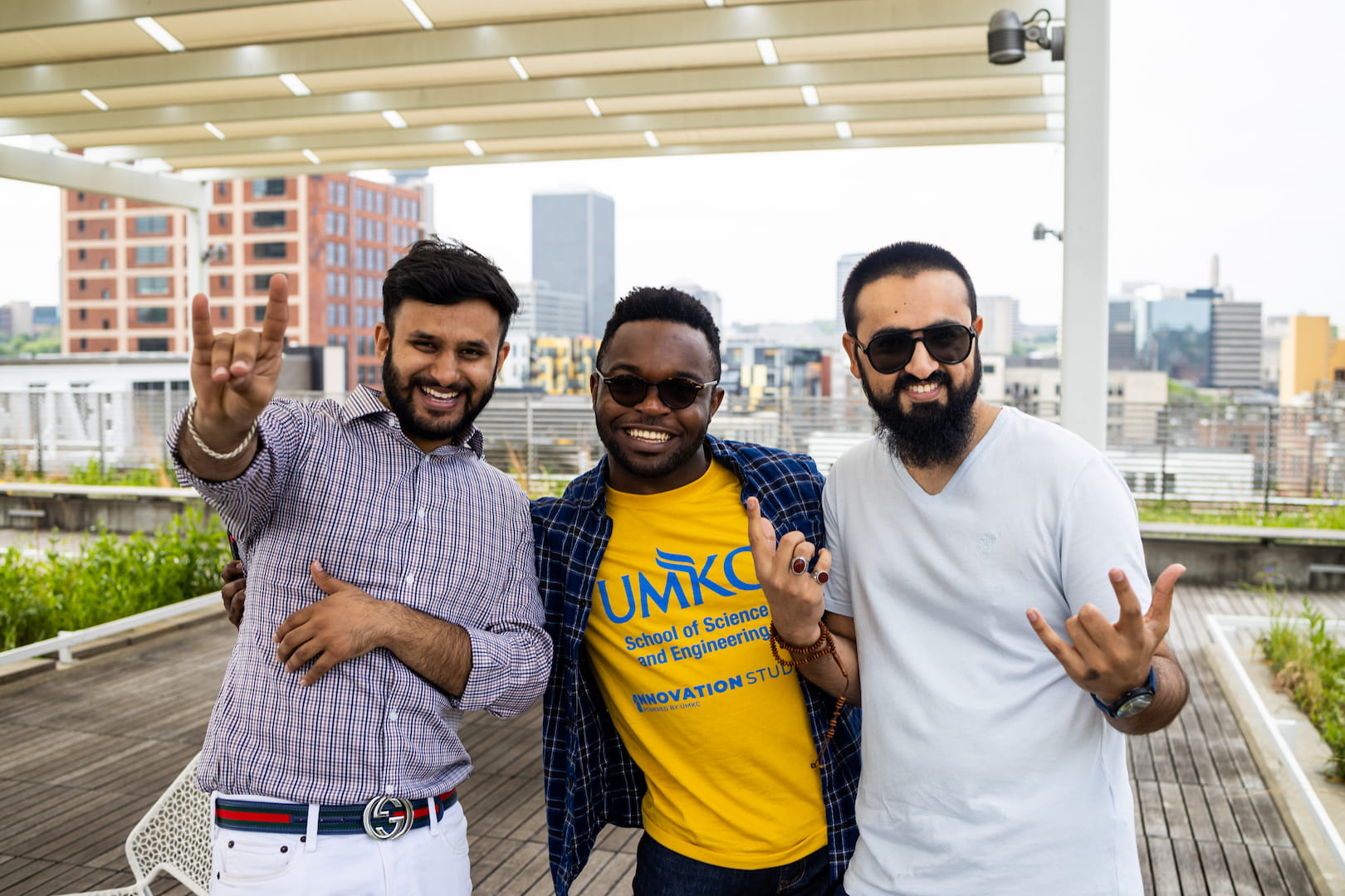 three students on the rooftop of Barkley link arms and flash the Roo Up hand sign