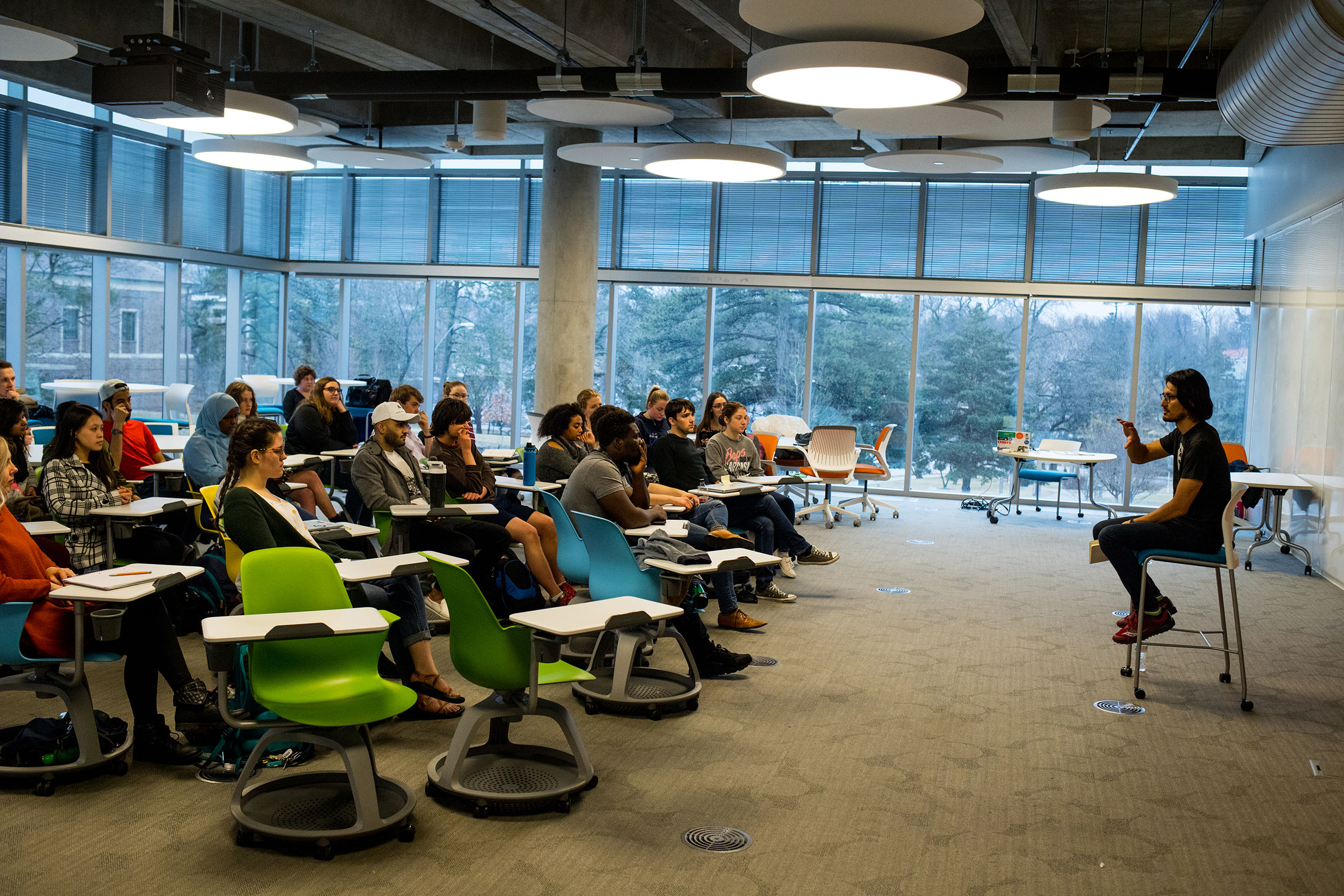 students sit in desks in classroom with teacher at front