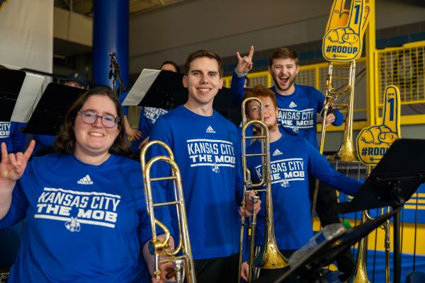 Members of the Mob, the 威尼斯人娱乐城 pep band, wear blue shirts and make the Roo Up hand sign in the stands for a basketball game at Swinney.