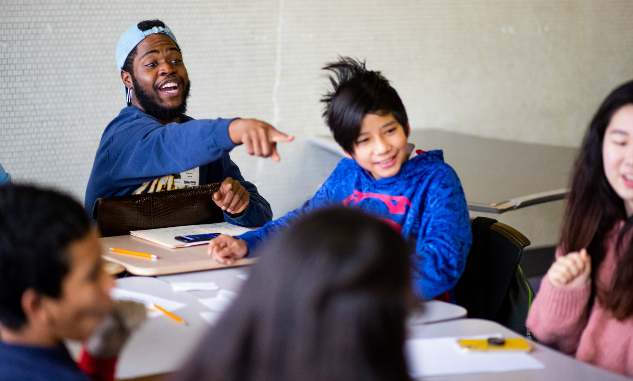 African American male education student excitedly interacts with diverse group of children in classroom setting