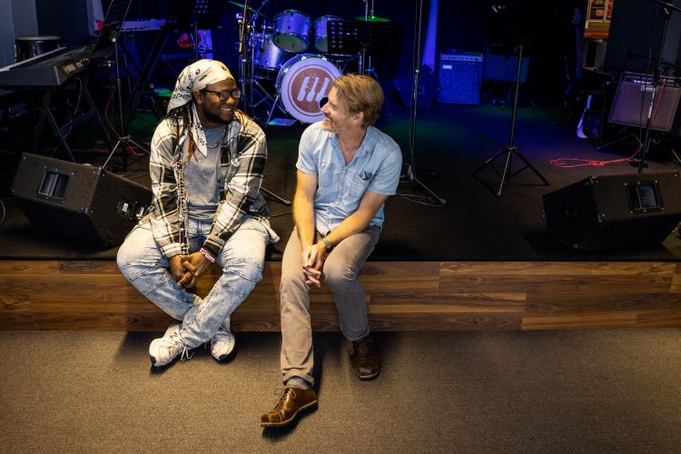 two people sit on the side of a stage, smiling