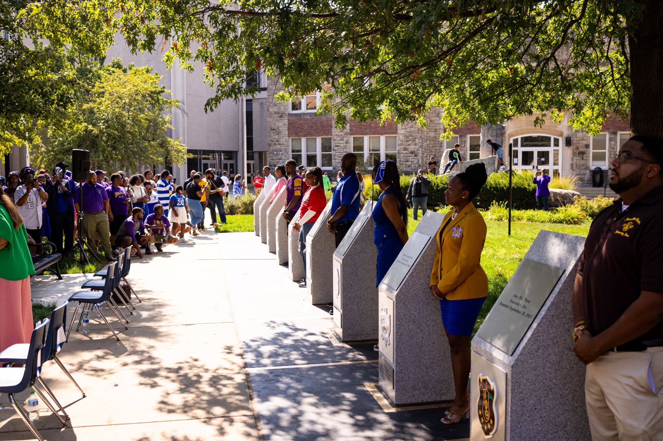 Representatives of the Divine Nine Black Greek organizations stand next to there fraternity's or sorority's plaque.