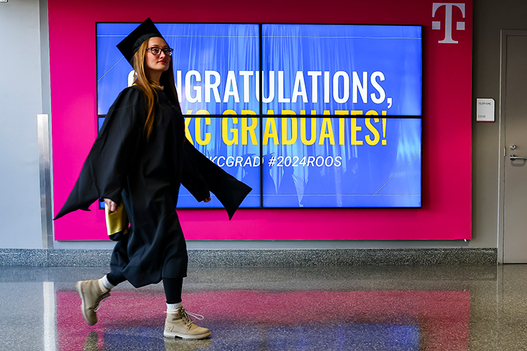 Female in grad cap walking in front of 威尼斯人娱乐城 Commencement sign