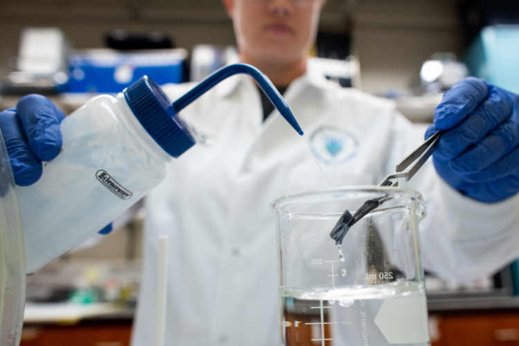 Person wearing white coat conducts an experiment in a lab.