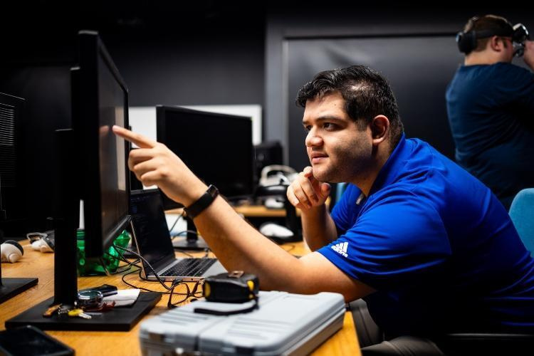 Person wearing blue shirt points to a computer screen.