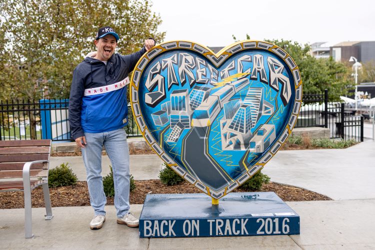 Ben stands beside his KC heart, smiling widely.