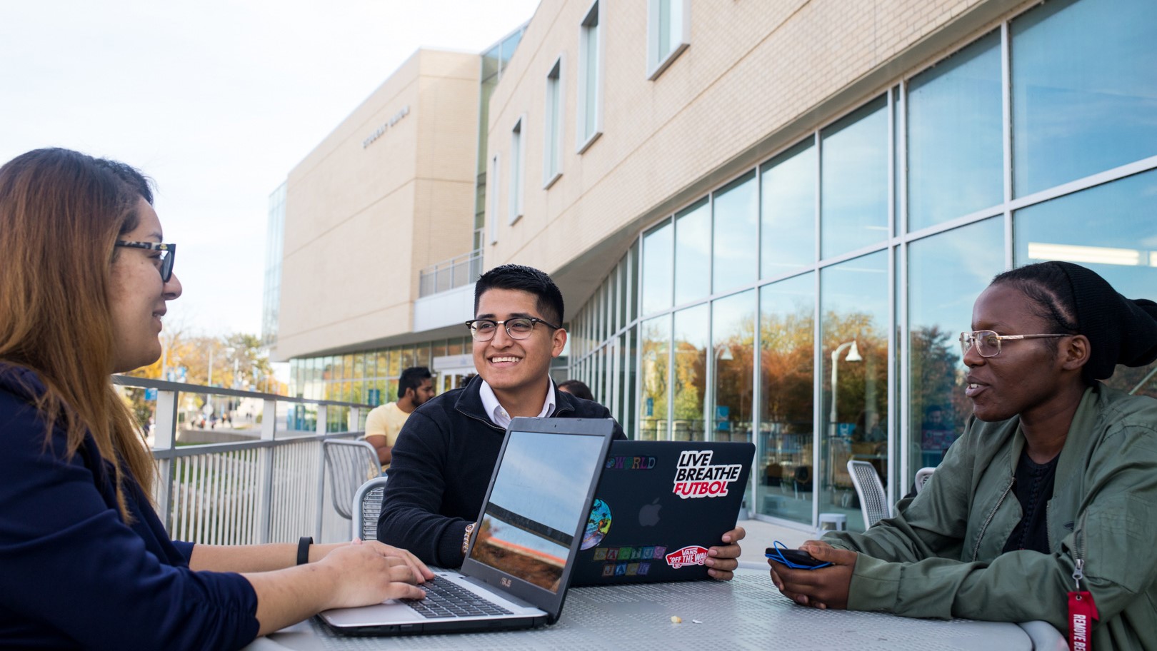 three students sit at a table with their laptops